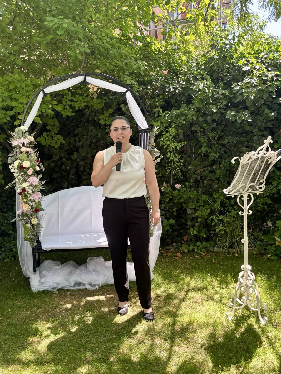 Freie Traurednerin Gayane Bock mit Mikrofon vor einem blumengeschmückten Traubogen